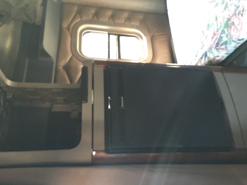 Freightliner Cascadia 125 truck cabin interior showing a compact refrigerator unit beside a small bed and window.
