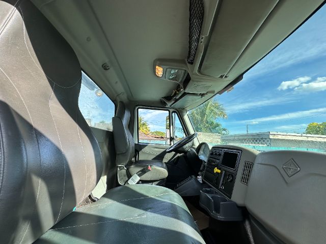 Truck interior cabin of a 2013 International 7500 showing driver seat, passenger seat, steering wheel, dashboard, and overhead controls. Clear sky visible through windshield.