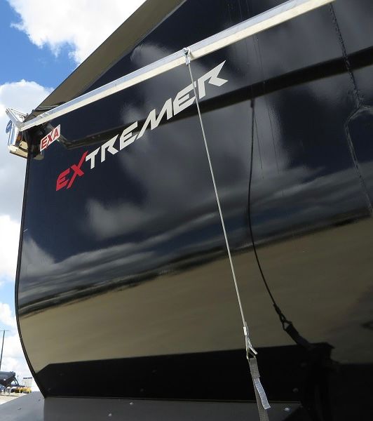 Extremely large glossy black dump trailer with EXTREMEK branding and rope tether visible on side.