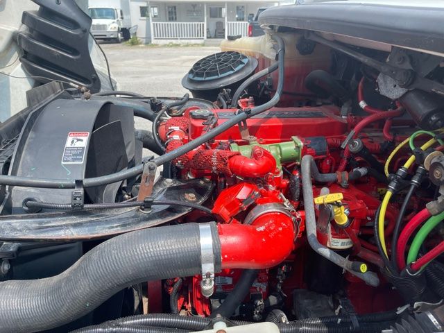 Freightliner M2 engine bay with red-painted components, hoses, and black air intake; various fluid reservoirs and electrical wiring visible.