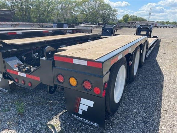 Fontaine 55 ton steel roller paver lowboy trailer rear view showing triple axle with wooden deck and black paint, Fontaine logo on mudflap.