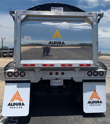 Aluminum end dump trailer with ALDURA TRAILER logos on rear, reflective tape, mud flaps, and license plate area.