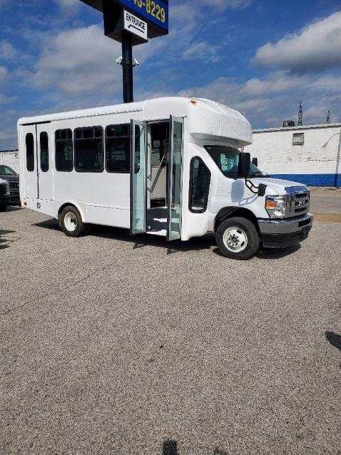Ford E450 shuttle bus side view showing open door and windows, white exterior, front grille, and dual rear wheels.