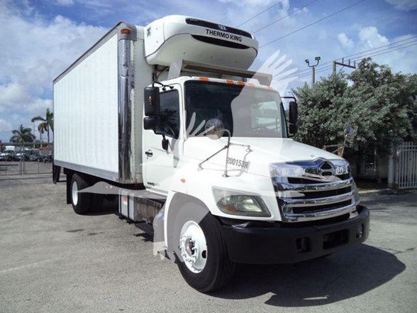 Truck with Thermo King reefer unit mounted on top, white box body, front grille with Hino badge, parked outdoors.