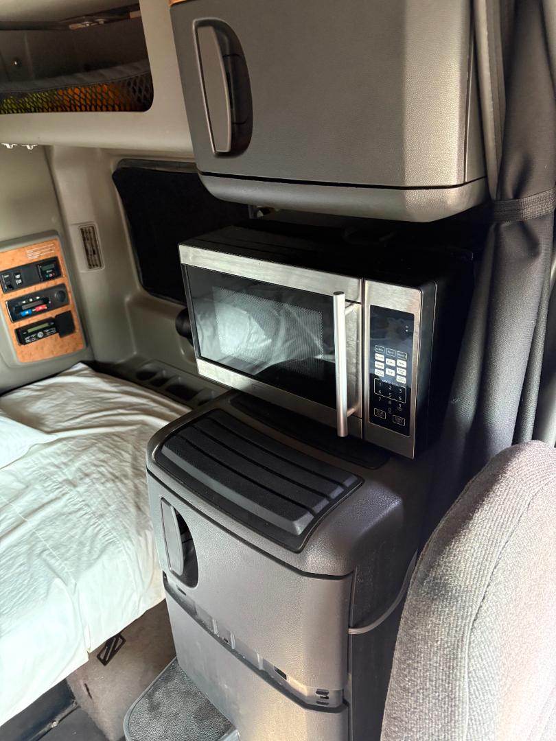 In-cabin view of a 2016 International Prostar with a stainless microwave mounted on a pedestal, adjacent to a control panel and storage drawer