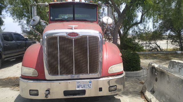 Peterbilt front view truck with large chrome grille, red cab, round mirrors, and California license plate WPL8192. Visible front bumper and headlights.