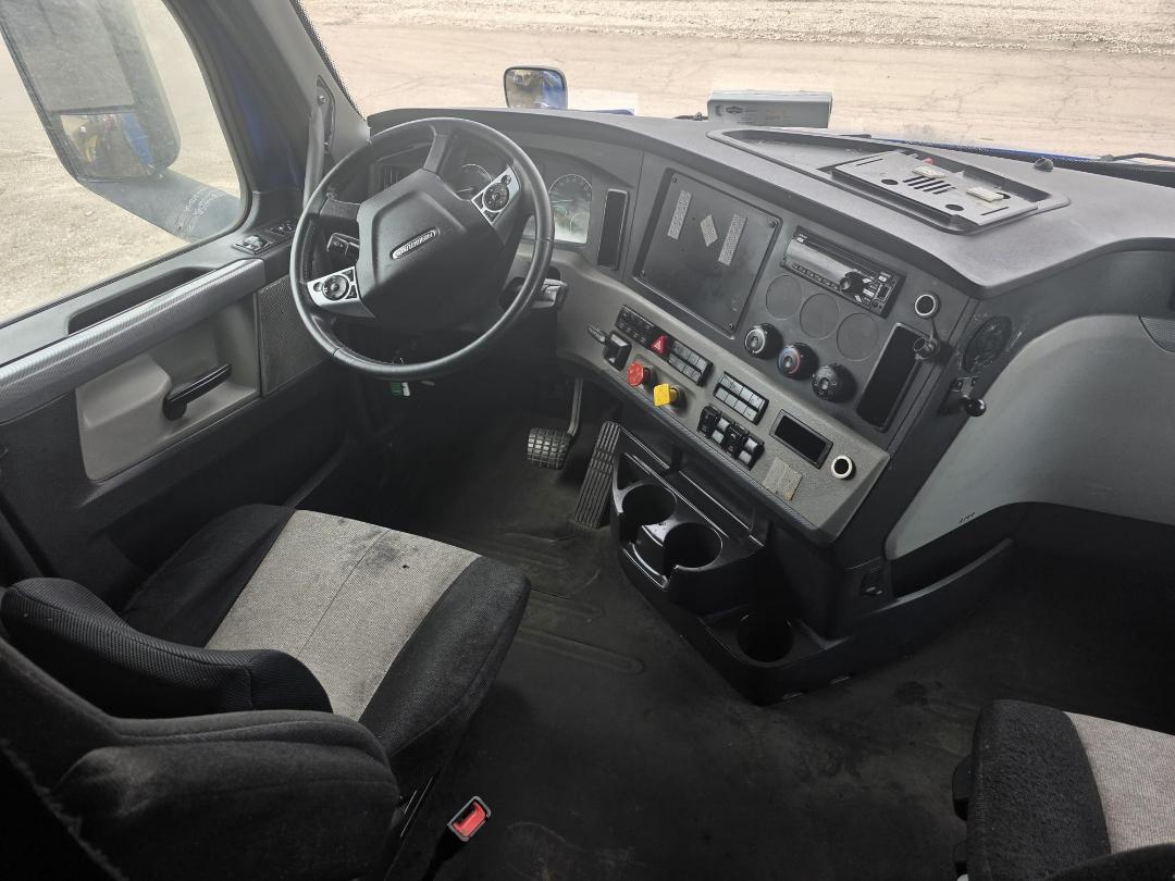 Cab interior of 2018 Freightliner Cascadia showing steering wheel, dashboard with gauges, center console, and cup holders.