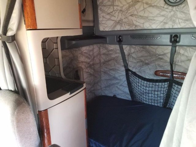 Cab interior of a Freightliner Cascadia sleeper showing storage cabinet, upper bunk area, and netted pocket.