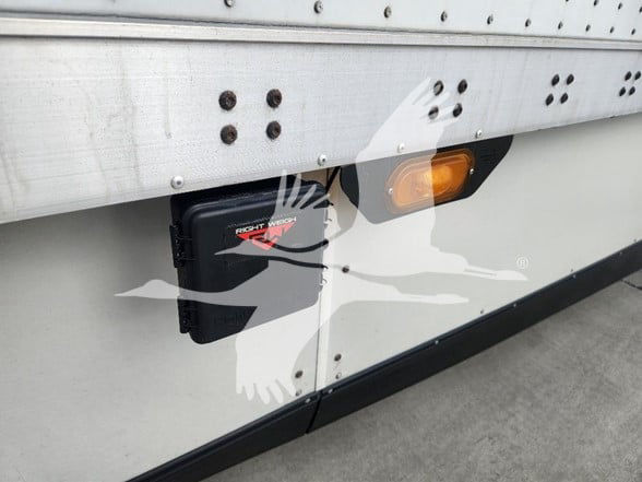 Rear side of a 2021 Wabash trailer showing a black Right Weight hydraulic landing gear housing and an orange marker light, aluminum side panel with rivets.