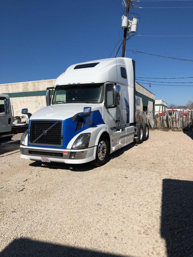 Volvo VNL64 tractor-trailer in a lot, front grille and headlights visible, white and blue paint with sleeper cab.