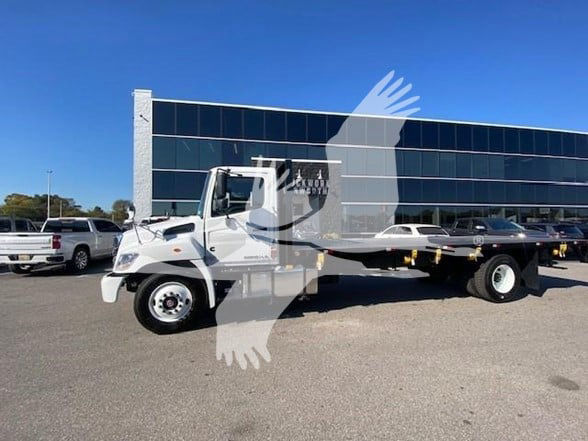 Flatbed tow truck side view showing white 2025 Hino L6 chassis with long steel bed in a dealership lot.