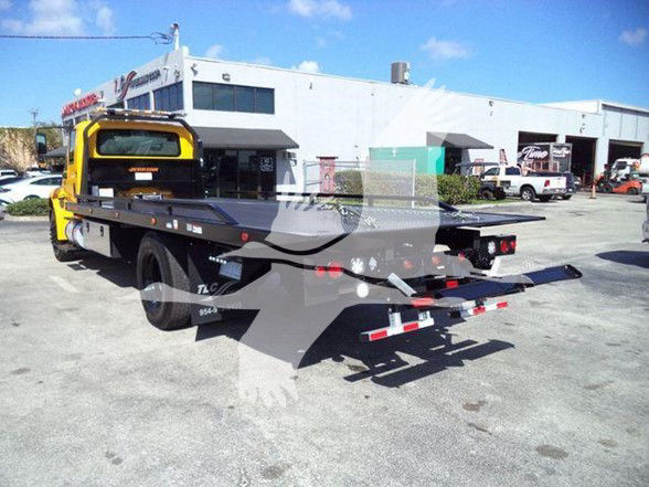 Tow truck flatbed with a yellow cab and white flatbed; rear view showing hydraulic equipment and tow bed.
