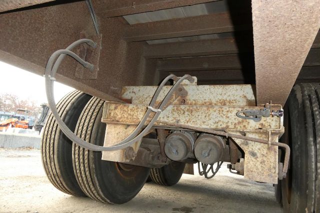 Trailer rear undercarriage showing dual wheels and suspension with rusted steel frame and electrical hoses.