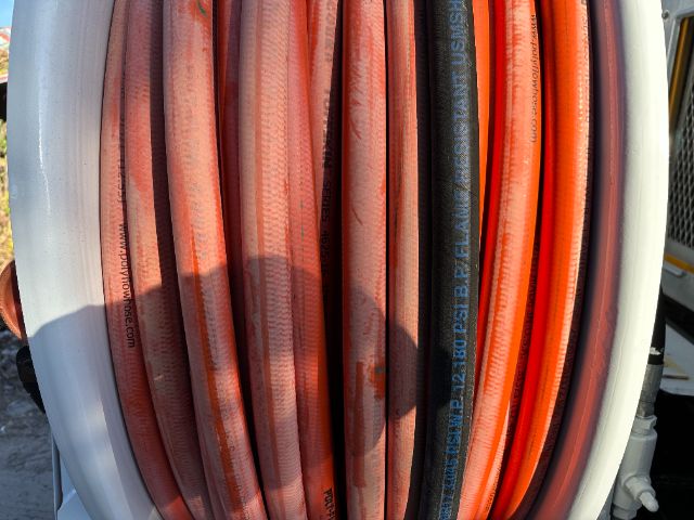 Assorted hydraulic hoses in a reel, with visible text on hoses including random brands and specifications; colors red, orange, and black.