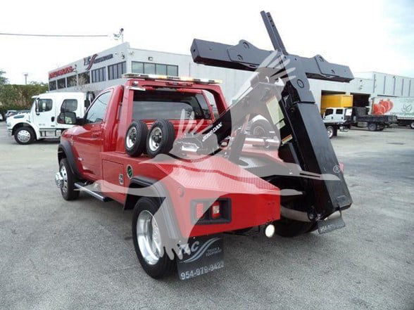 Tow truck with a mechanical lift in a raised position, red cab, spare wheel on door, and black load bed.