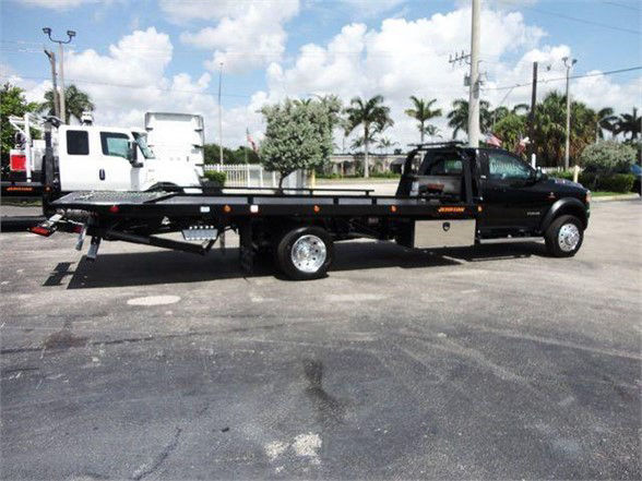 2024 Ram 5500 SLT tow truck side view with long flatbed and black color showing chrome wheels and rear equipment.