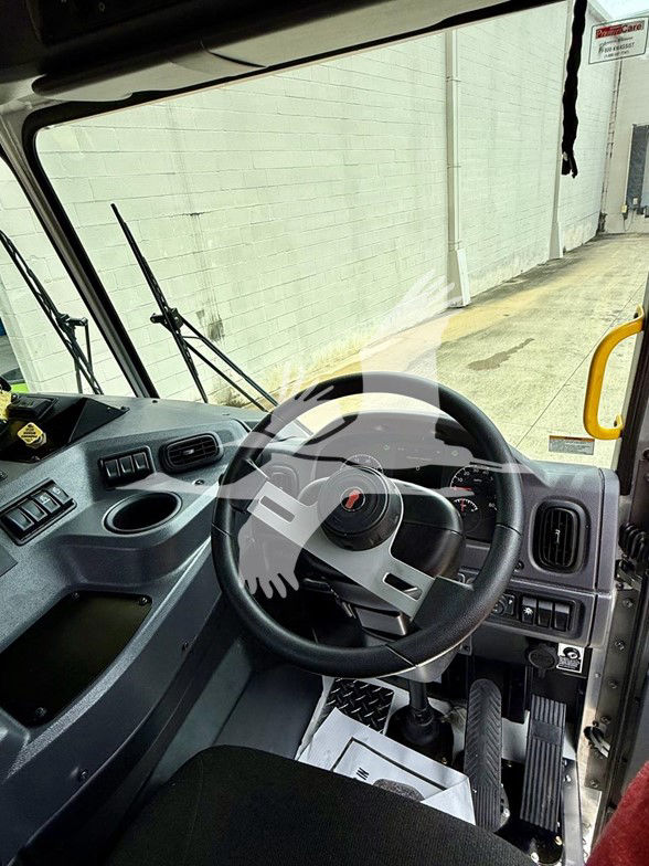 Kenworth L770 cab interior showing steering wheel, dashboard, pedals, and driver’s seat. Cockpit with gear lever, control panels, and windshield view.