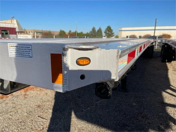 Flatbed trailer corner showing aluminum frame, side marker light, and wheel stop; label plate visible.