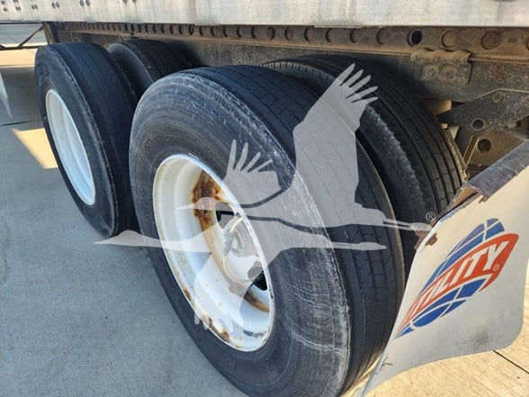 Trailer axle wheels showing dual tires and white rims under a Wabash trailer. Visible rust on wheel hub and side skirt with logo.
