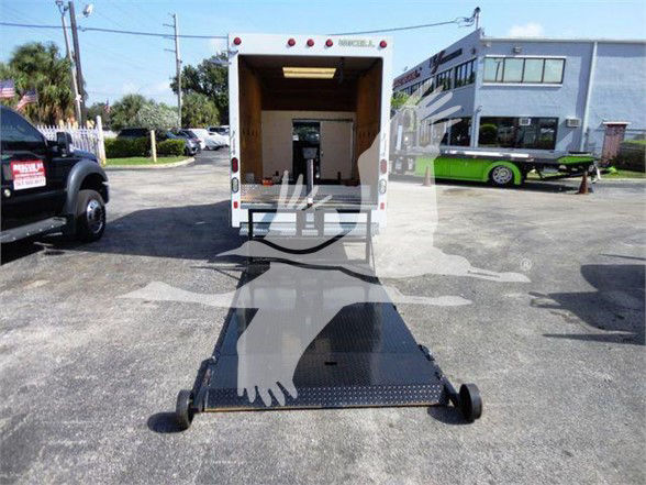 Ford E-Series box truck with rear ramp lowered for loading/unloading in a parking lot.