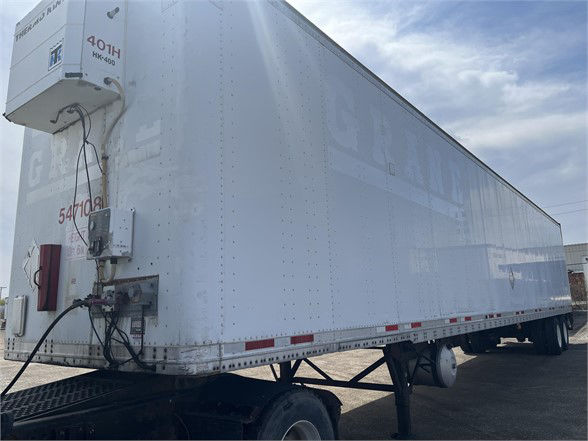 Wabash dry van trailer with reefer unit at front left, side panels riveted, white exterior, trailer on a flatbed dolly.