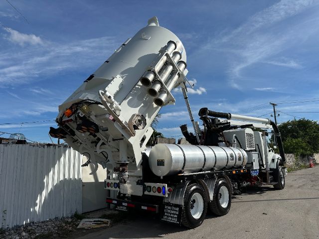 2013 International 7500 vacuum truck with elevated silo/mixer and hoses mounted on a flatbed, rear view showing cylindrical tank and hydraulic equipment.
