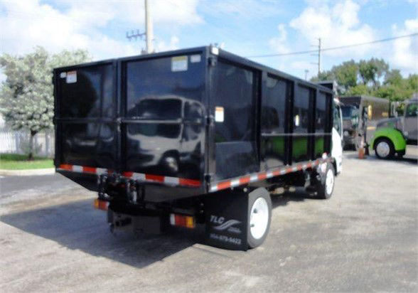 Isuzu NPR HD dump truck rear/side view showing black dump bed and white cab, with TLC branding on rear wheel area.