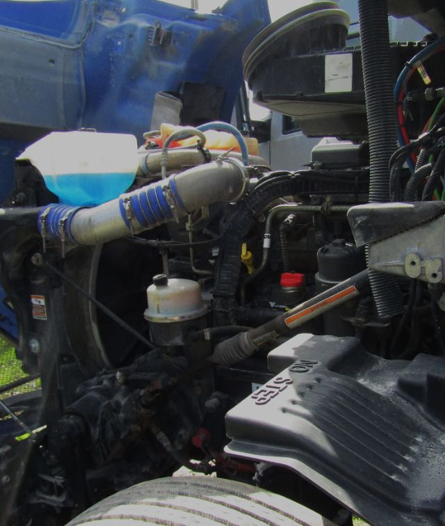 Kenworth T680 engine bay showing coolant reservoir with blue liquid, hoses, and various engine components.