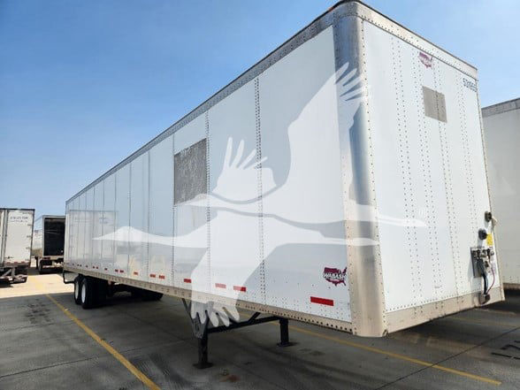 White Wabash trailer in a parking lot with dual rear doors and support legs, side riveted panels, and a small logo near the rear.