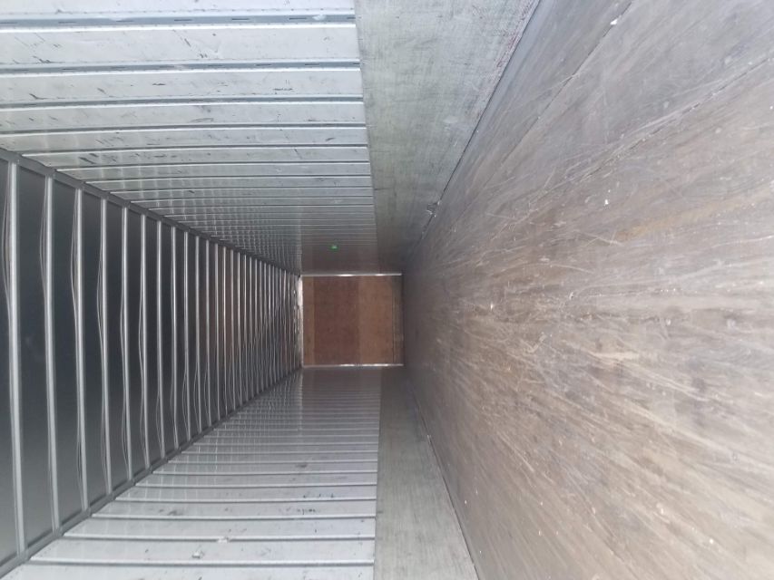 Interior of a cargo trailer showing metal walls, ribbed ceiling, wooden floor, and a rear wall.