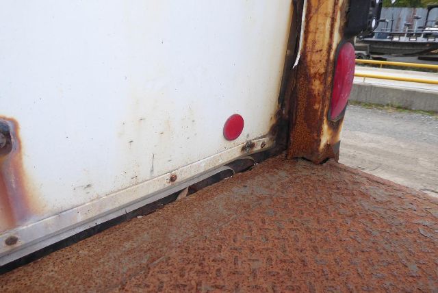 Truck cargo area with rusted edge and white body panel showing a small red reflector.