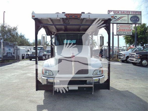 Kenworth T370 truck in a car carrier setup, front view with loading ramp frame overhead, dealership lot in background.