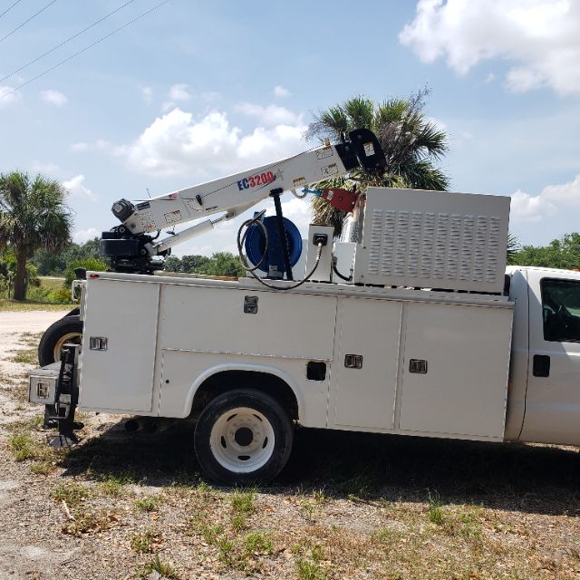 Utility truck with a bucket crane mounted on the bed, compartments along the side, and a rear wheel visible.