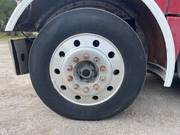 Front wheel of a Peterbilt truck showing a silver multi-hole hub and lug nuts. No visible text legible other than wheel details.