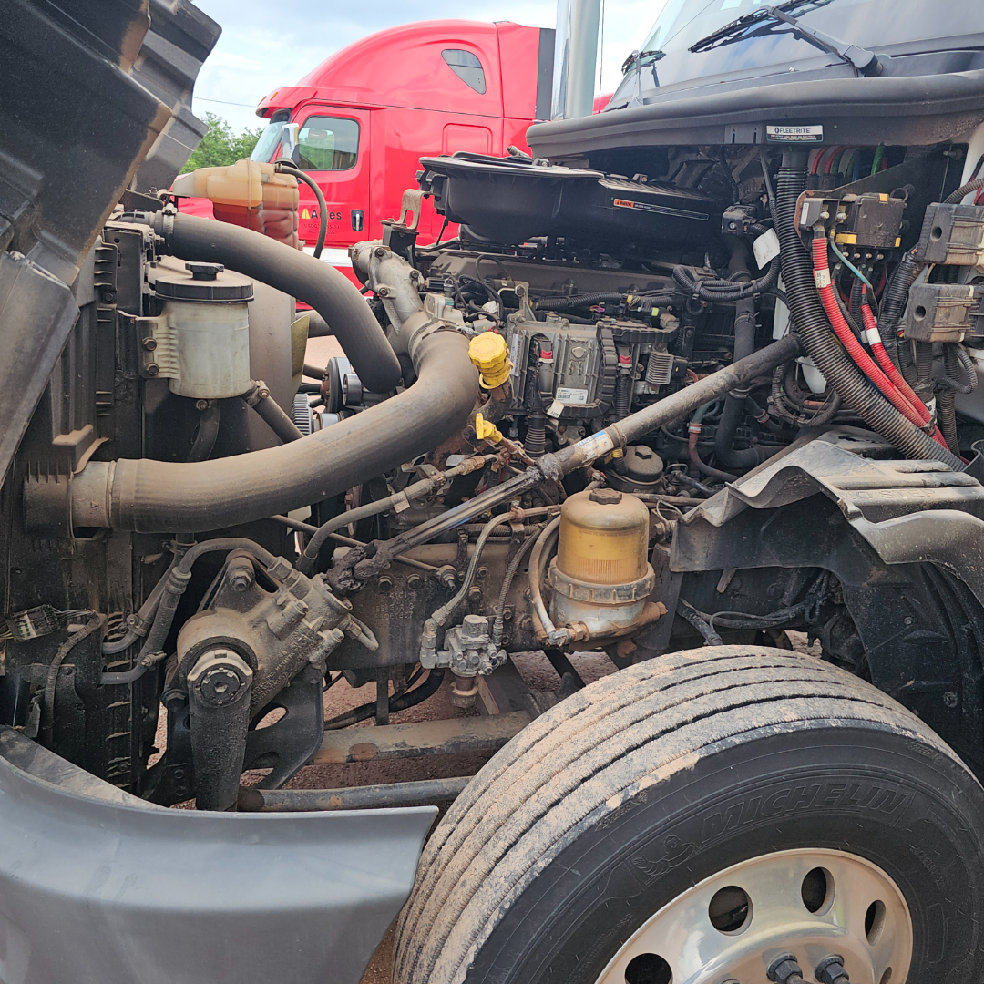 International LT engine bay showing hoses, yellow oil fill cap, air filters, and wiring harness; front left wheel and chassis components visible.