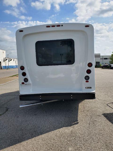 Rear view of a white 2025 Ford E450 shuttle bus showing taillights, rear window, and bumper with hitch step.