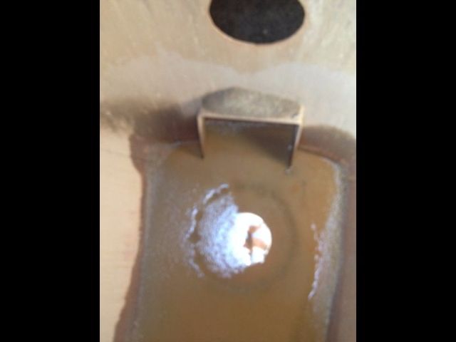 Industrial equipment interior showing a brown tank cavity with a circular hole surrounded by white residue. A rectangular tab or bracket is visible at the top inside.