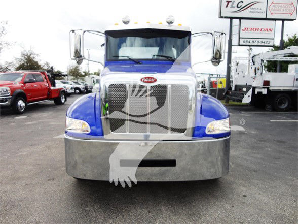 Peterbilt 337 front view showing large chrome grille, blue cab, and bumper. Visible text includes Peterbilt emblem on grille. Background signage and surrounding trucks.
