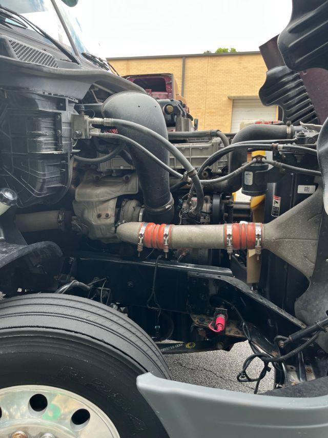 Freightliner Cascadia engine bay with visible turbo intake pipes, radiator hoses, and a red-orange hose clamp; front wheel and suspension components visible; engine bay view.