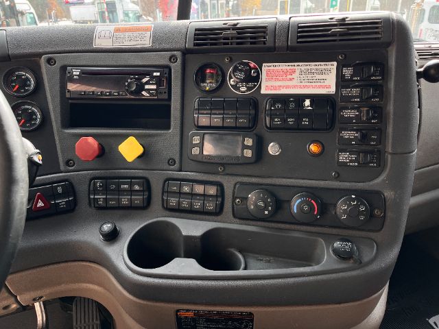 Cab interior of a Freightliner Cascadia truck dashboard showing various gauges, buttons, and control switches.