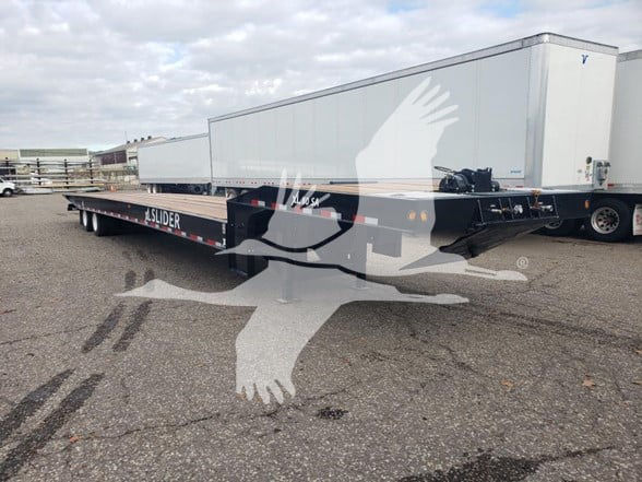 Trailer chassis showing 'SLIDER' branding on the frame, flatbed with multiple axles, and a white refrigeration trailer in background.