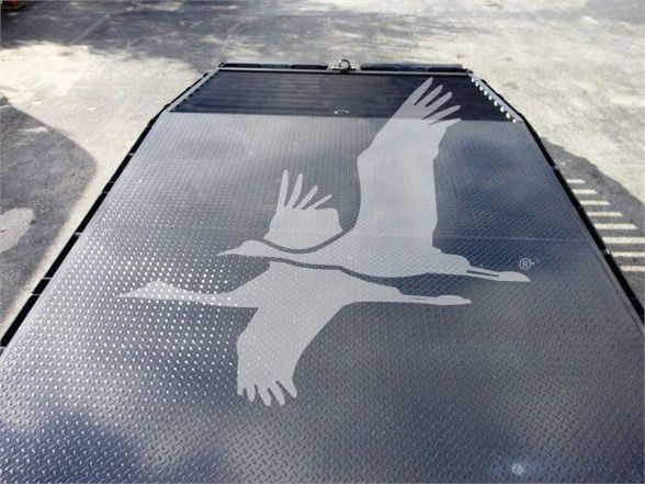 Flatbed truck bed with diamond plate surface featuring a large white graphic of a flying bird logo.