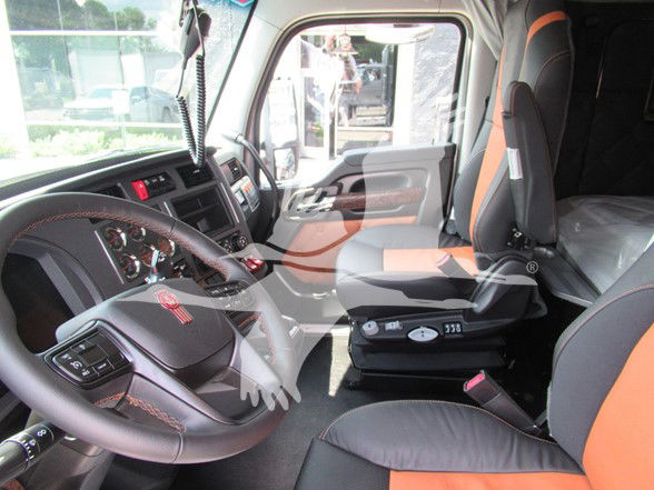 Kenworth W990 truck cabin interior showing steering wheel with Kenworth emblem, dashboard controls, and orange/black seats.