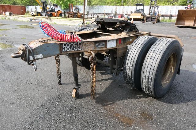 Trailer dolly chassis with red and blue coiled air line, two large rear tires, ladder frame, and chains. Visible plate reads 58255. Background shows industrial yard.