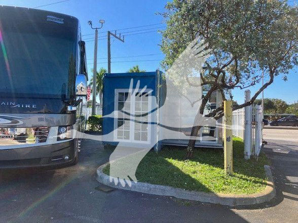 Truck trailer with blue container and RV parked adjacent, with a large translucent overlay graphic in the foreground and a gray bus to the left.