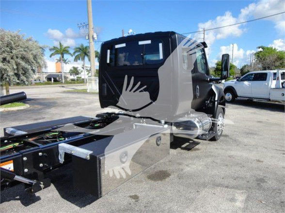 Vehicle chassis with cab and mounting for a heavy tow truck, side view showing black and gray body panels, wheel, and rear frame with mounting platform.