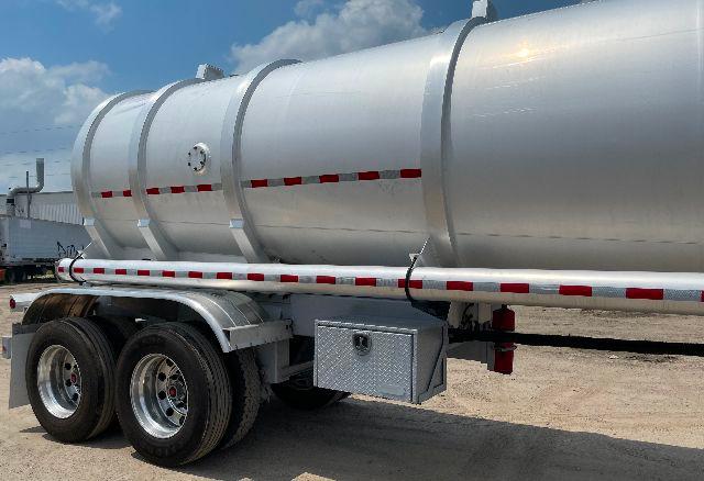 Aluminum DOT-407 crude oil tanker trailer showing side view with dual rear axles and storage toolbox.