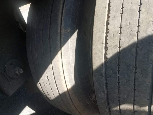 Truck trailer tires side-by-side, tread wear visible, wheel hub and suspension area partially visible.