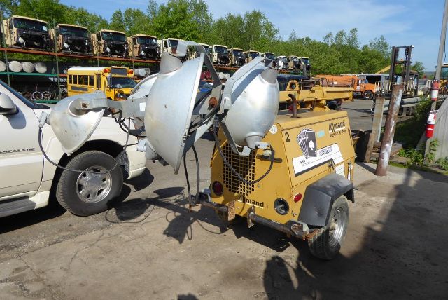 Allmand Night Lite Pro portable lighting tower attached to a yellow trailer in a yard with other equipment in the background.