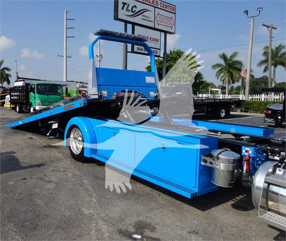 Blue Peterbilt 337 flatbed truck with hydraulic ramp and dual axles in a dealership lot.